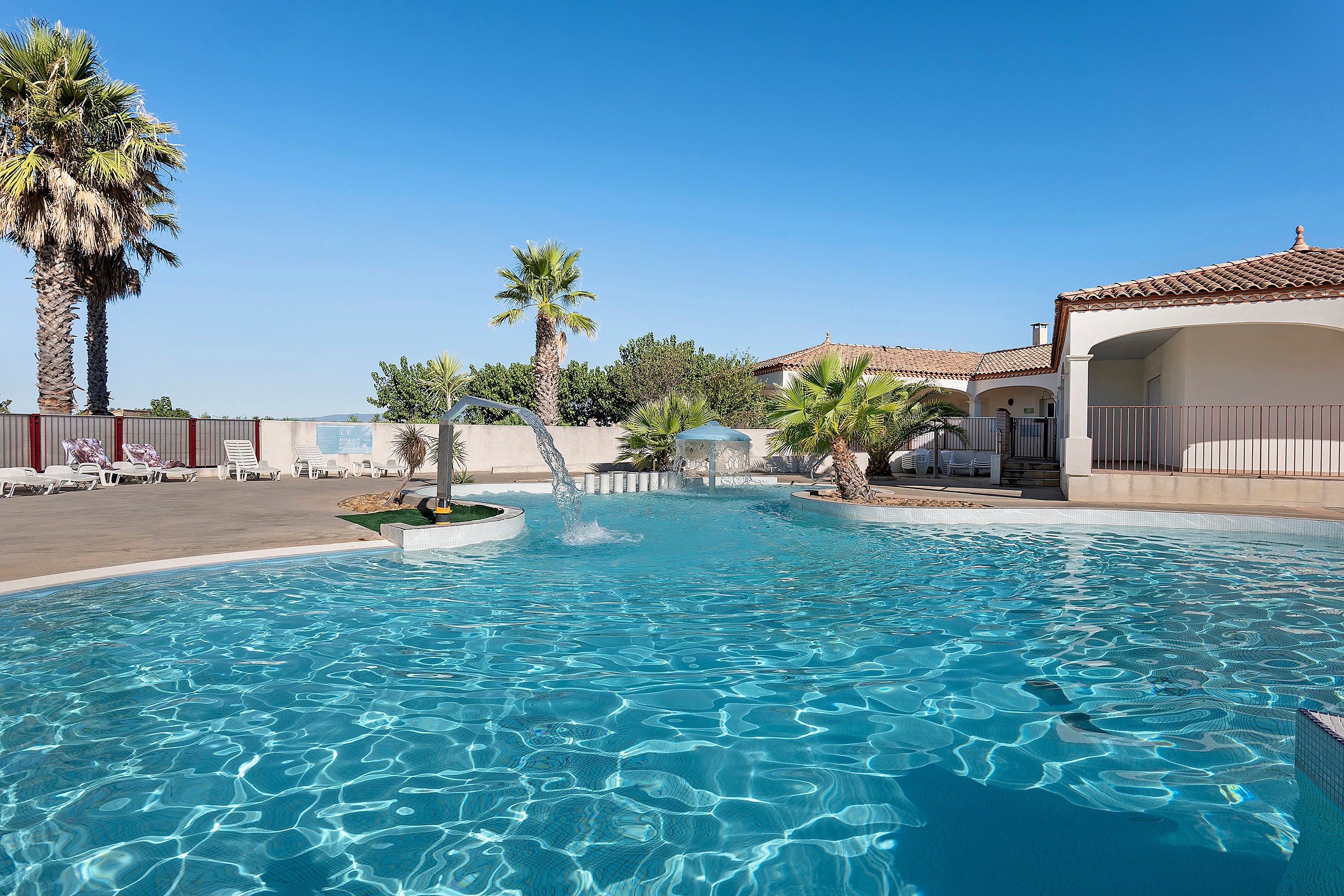 A clear blue pool with palm trees and lounge chairs around it.