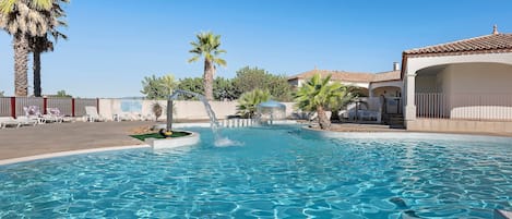 A clear blue pool with palm trees and lounge chairs around it.