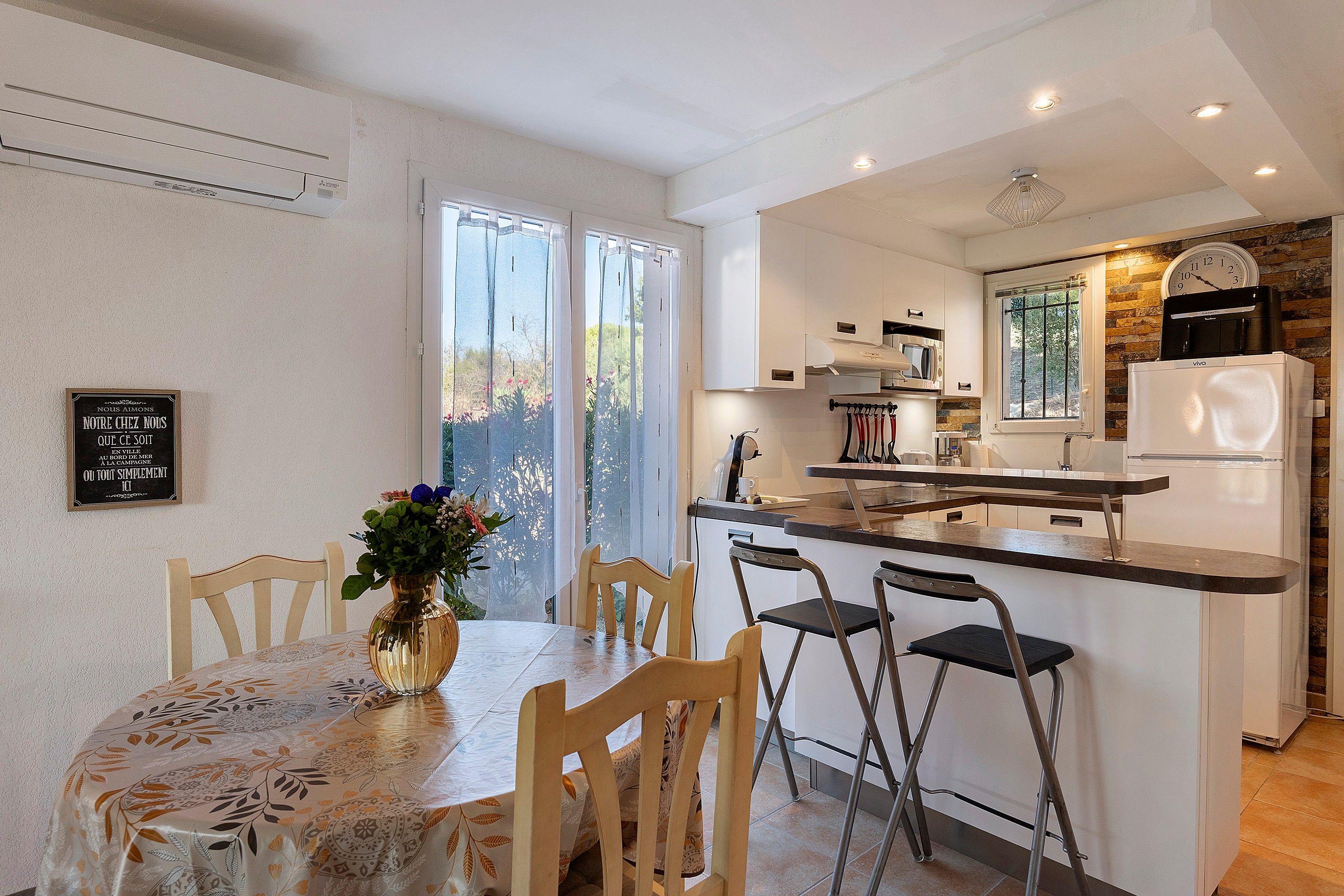Cocina moderna con una isla central, armarios blancos y una zona de comedor con mesa y sillas.