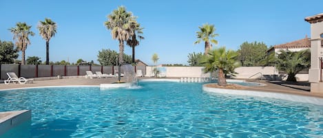 A swimming pool with clear blue water, surrounded by palm trees and lounge chairs.