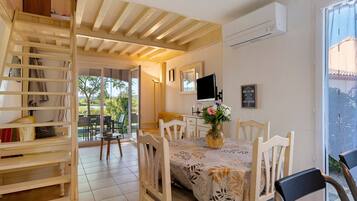 Un comedor con una mesa lista para cuatro, un televisor montado en la pared y una ventana con vista a follaje.