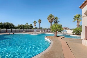 Una piscina con agua azul cristalina, rodeada de palmeras y un deck de baldosas.
