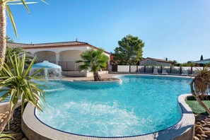 A swimming pool with a fountain, surrounded by palm trees and a fence.