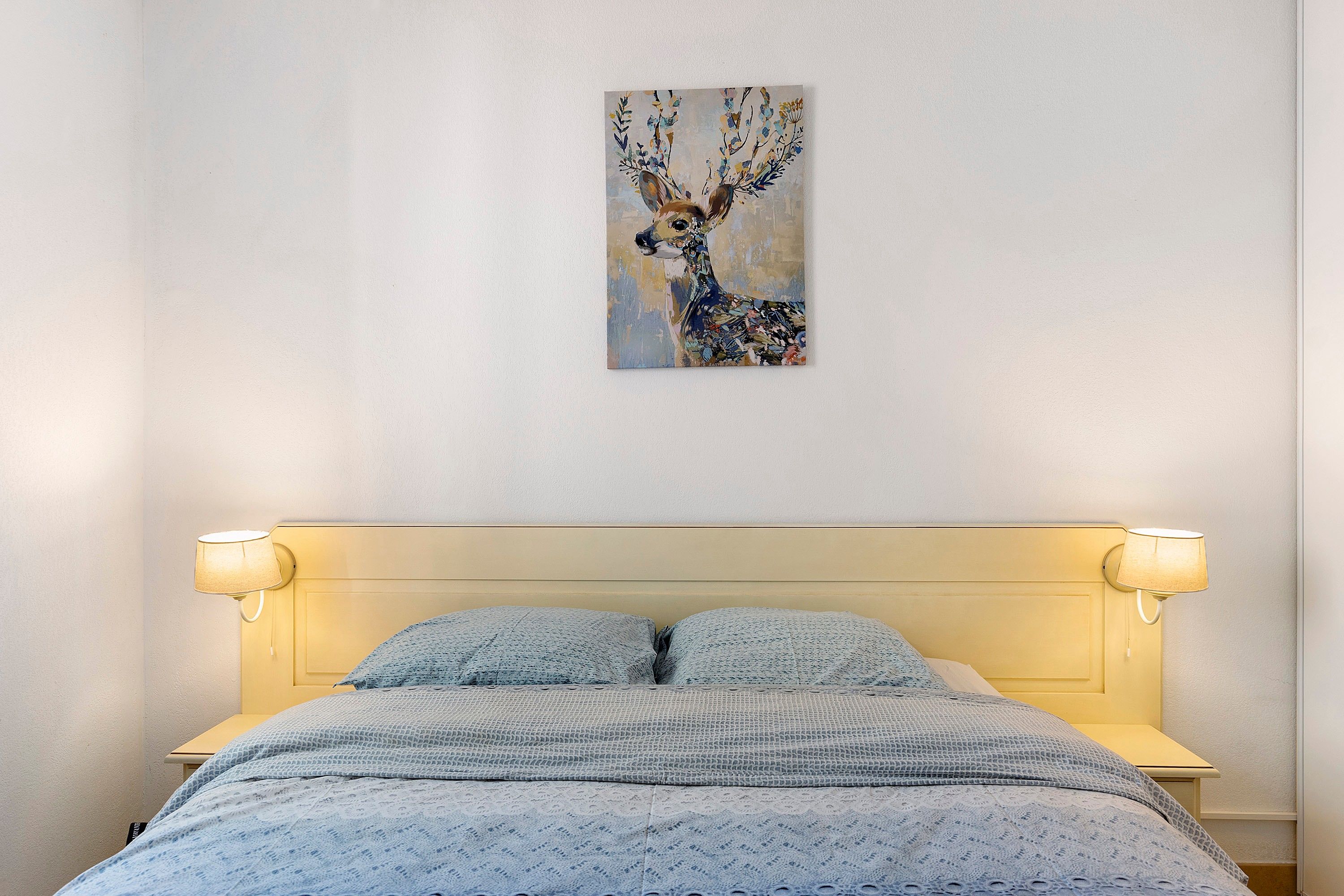A bed with a headboard, two bedside lamps, and a wall-mounted painting of a deer.