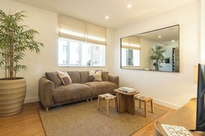 A living room with a sofa, a coffee table, a small side table, a large mirror, and a potted plant. - Sea'Ya Cascais – Apartment in the Heart of Cascais (Cascais)