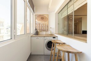 Un área de lavandería compacta con lavadora, tendedero y ventana con vista a edificios.