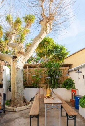 Eine Terrassenfläche mit einem Holztisch und Bänken, umgeben von einem Bambuszaun und verschiedenen Pflanzen.
