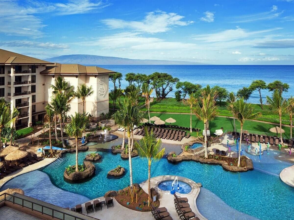 Een zwembadgedeelte van een resort met diverse waterattracties, ligbedden en uitzicht op de oceaan.
