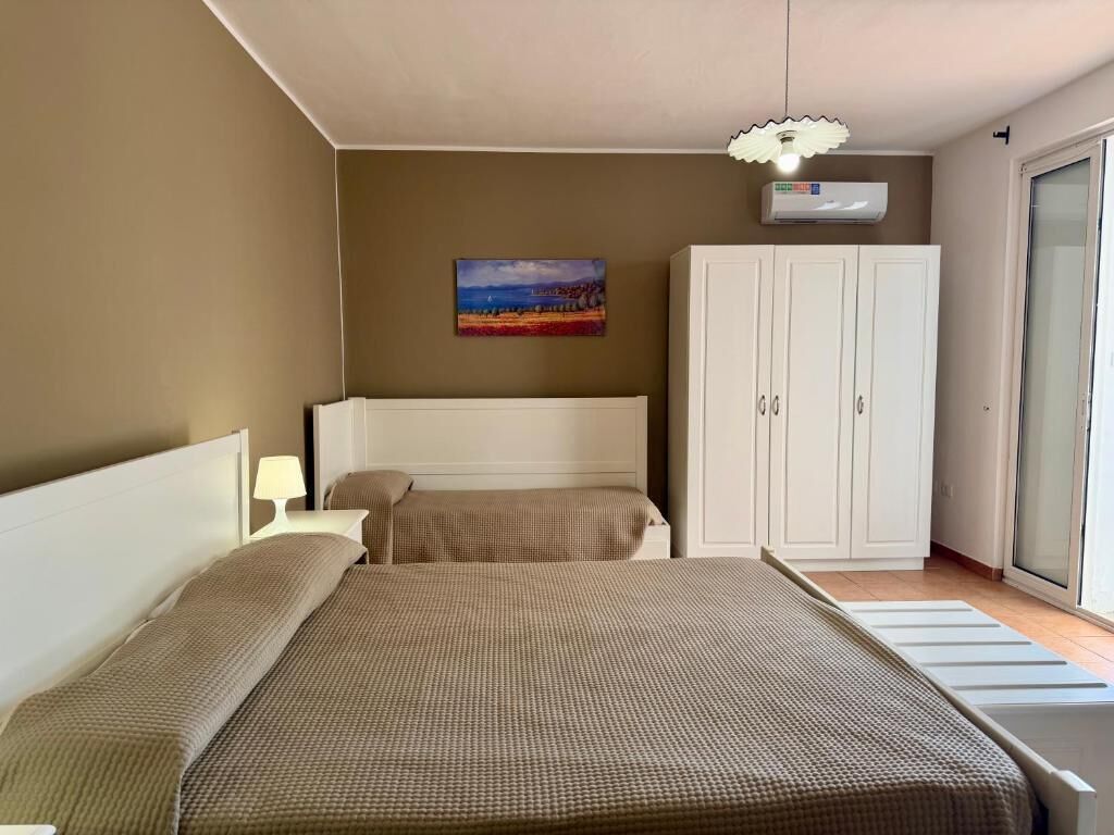 A bedroom with a bed, a wardrobe, a painting on the wall, and a ceiling light fixture.