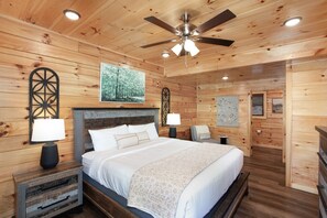 Ein Schlafzimmer einer Holzhütte mit einem Bett, Nachttischen, einem Deckenventilator und Wandbildern.