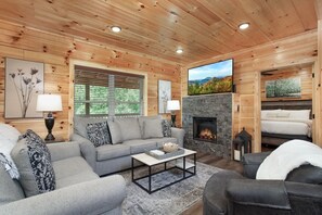 Ein gemütliches Blockhaus-Interieur mit Kamin, einer Couch, einem Couchtisch und einem Bett.