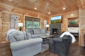 Ein gemütliches Blockhaus-Interieur mit Kamin, einer Sofagarnitur und einem Fernseher.