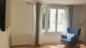 A room with a blue armchair, a radiator, a window with curtains, and a lamp.