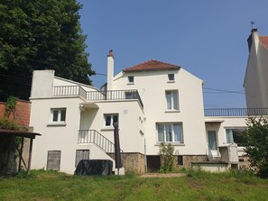 A two-story building with a balcony, a chimney, and a small garden area. - Cottage 'Gîte' with Private Garden, Balcony and Wi-Fi (Essômes-sur-Marne)