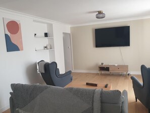 A living room with a flat-screen TV mounted on the wall, a wooden coffee table, and two grey armchairs. - Cottage 'Gîte' with Private Garden, Balcony and Wi-Fi (Essômes-sur-Marne)