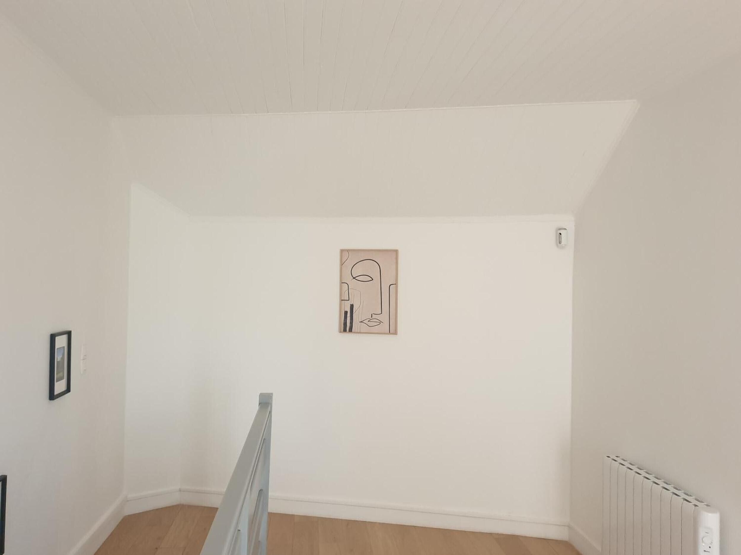 A room with a sloped ceiling, a radiator, and a framed artwork on the wall.