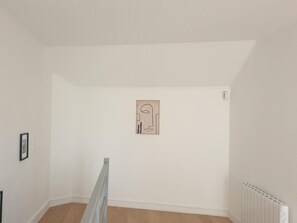 A room with a sloped ceiling, a radiator, and a framed artwork on the wall.