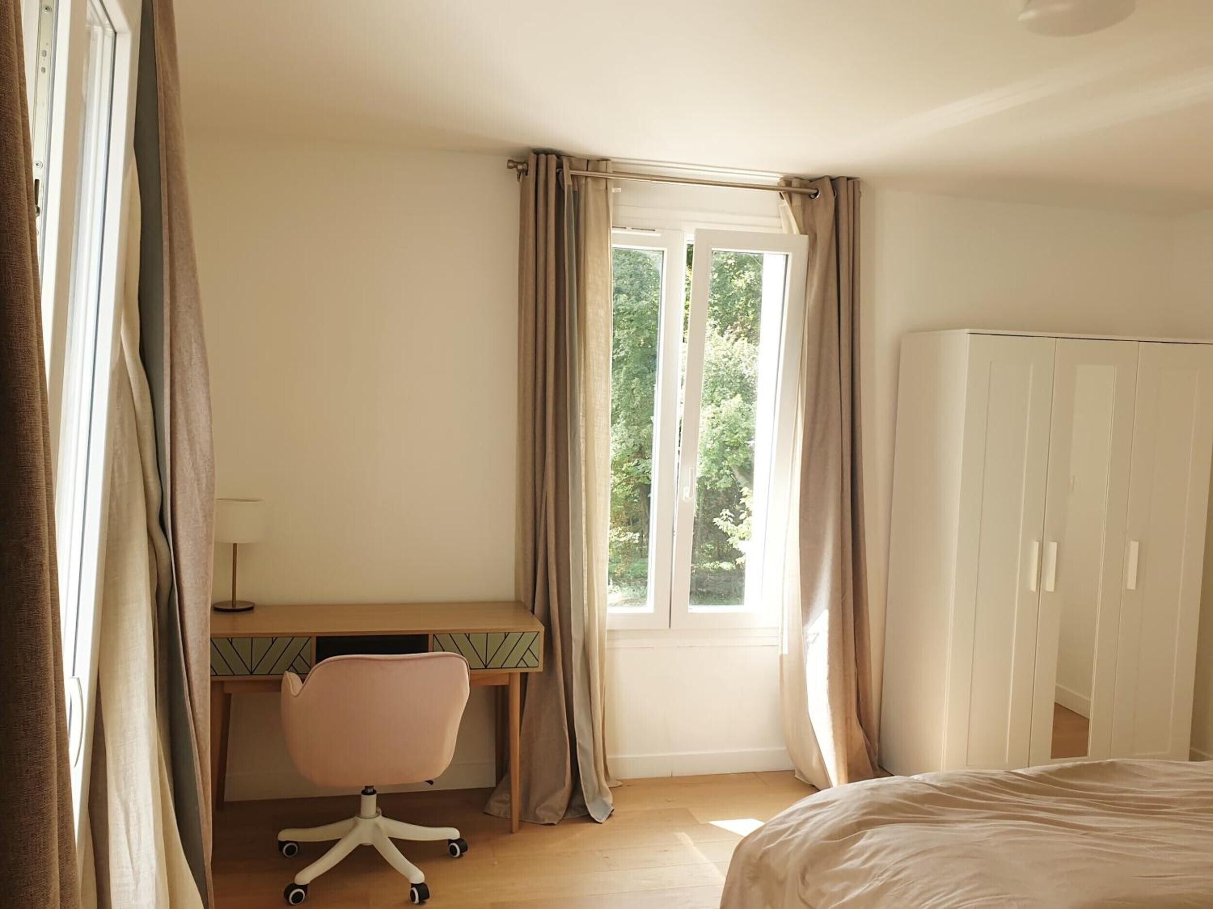 A bedroom with a bed, a desk with a chair, a wardrobe, and a window with curtains.