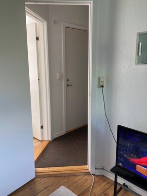 A room with a television on a stand, a door leading to another room, and a carpeted floor.
