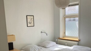 Ein Schlafzimmer mit Bett, Nachttisch, Lampe, Heizkörper und einem Fenster mit Blick.
