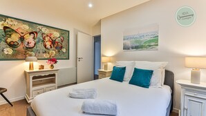A hotel room with a large bed, two bedside tables, a nightstand, a painting on the wall, and a window with a view. - Boreal - Maison Saint Gilles Croix de Vie (Saint-Gilles-Croix-de-Vie)