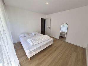 Una habitació amb un llit individual, una porta, un mirall i una finestra.