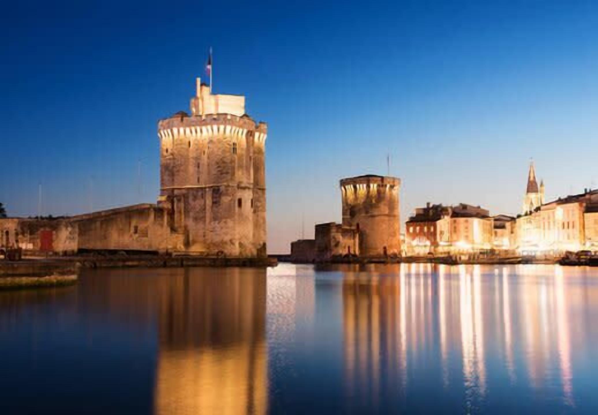 A historic waterfront cityscape with prominent fortifications and a clear reflection in the water.