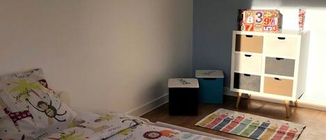Un dormitorio infantil con una cama, un mueble de almacenaje y una mesita.