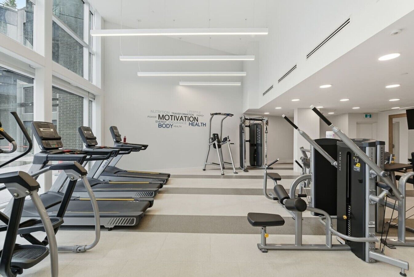 Une salle de sport moderne équipée de tapis de course, d’appareils de musculation et d’un mur d’inspiration.