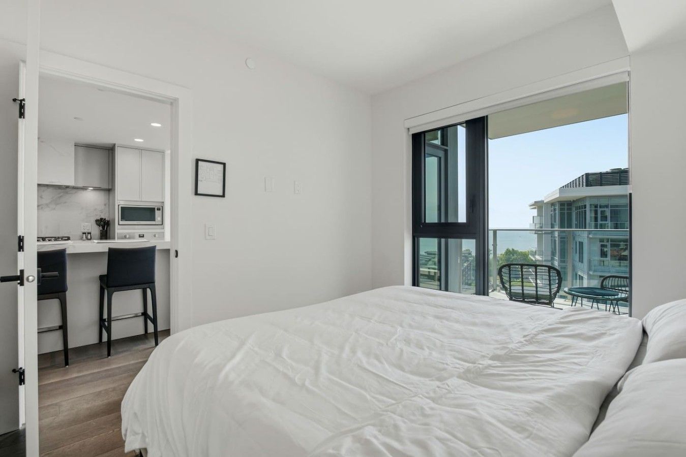 A bedroom with a large bed, a desk with a chair, and a balcony with a view.