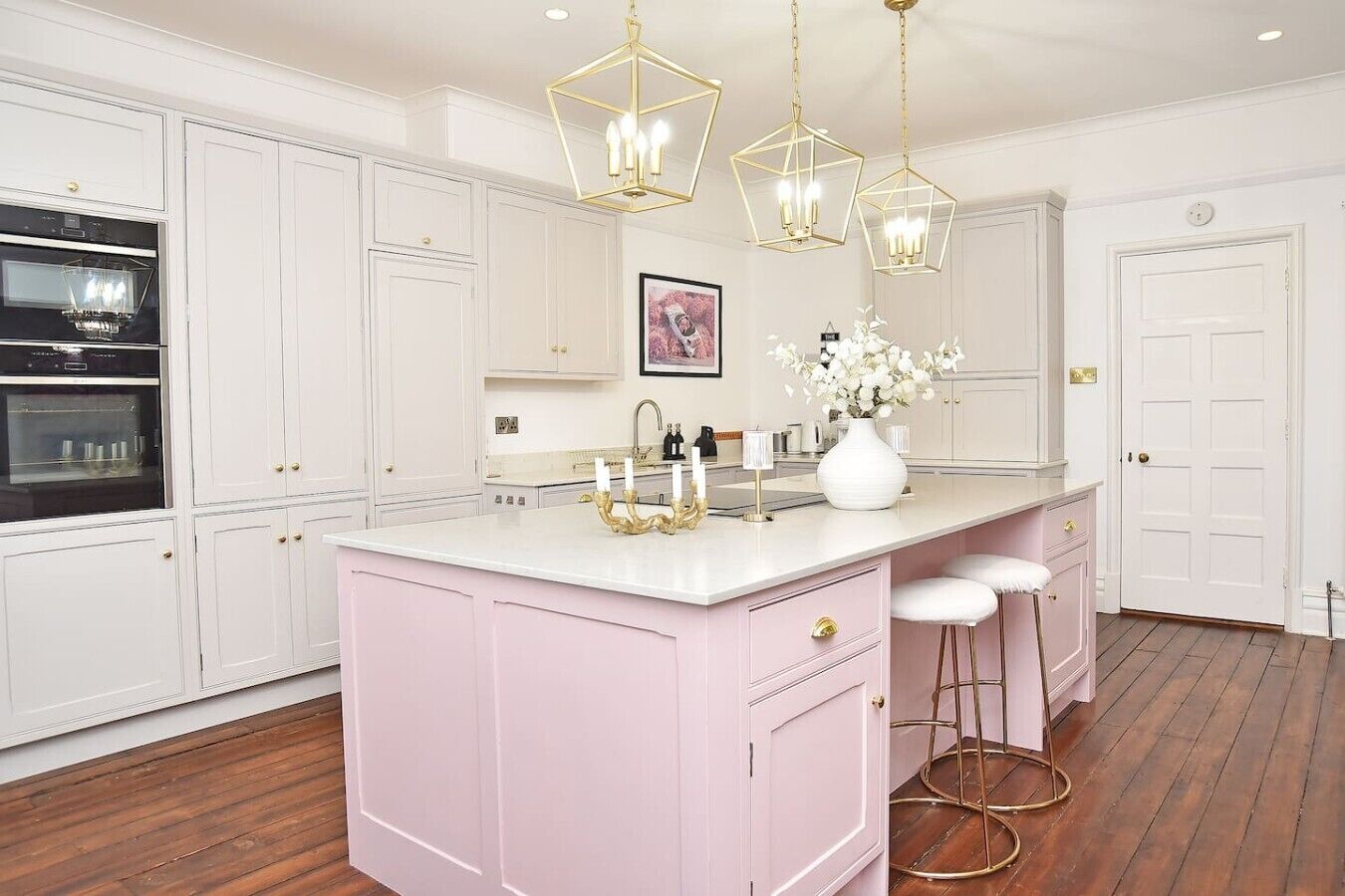 Una cucina con mobili bianchi, un'isola rosa e lampade a sospensione dorate.