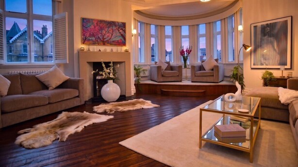 Ein geräumiges Wohnzimmer mit Kamin, Ledersofas, einem Glastisch und großen Fenstern.