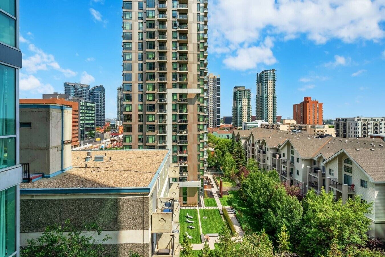 A high-rise residential building with multiple balconies, surrounded by other high-rise buildings and a well-maintained green space.
