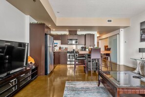A modern kitchen with stainless steel appliances, a dining area with a glass table, and a TV on a wooden stand. - 2 Bed 2 Bath | Mins to Stampede | AC (Calgary)