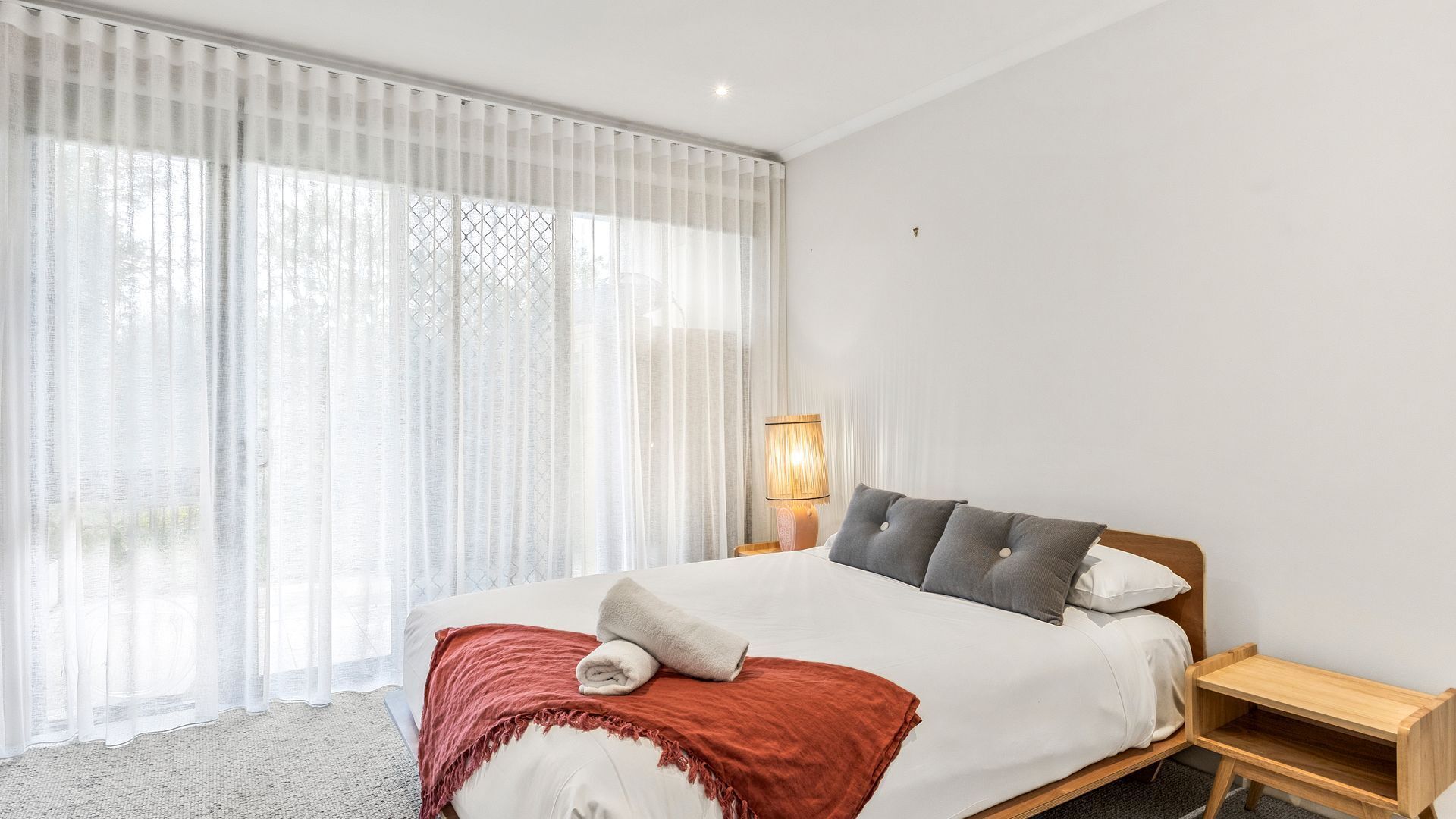 A bedroom with a large bed, a bedside table, a lamp, and sheer curtains.