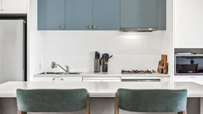 Eine moderne Küche mit weißer Arbeitsplatte, Edelstahlgeräten und blaugrünen Stühlen.