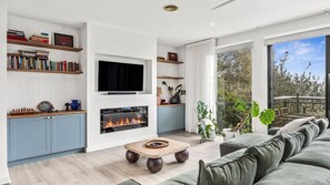 A modern living room with a fireplace, bookshelves, a television, and a view of the outdoors. - Coastal Resort Style Living Golf Tennis Pool & Beach (Torquay)