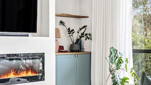 Ein Wohnzimmer mit Kamin, einem blauen Schrank und einem Fenster mit Vorhängen.
