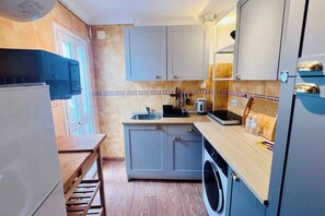Une cuisine de taille réduite équipée d’un lave-linge, d’un évier et d’une cuisinière.