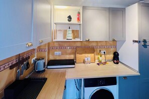 A compact kitchenette with a coffee maker, kettle, and a small countertop with bottles and a wine bottle. - Cozy Historical Andalusian 3BR House Peachy Stays (Mijas)
