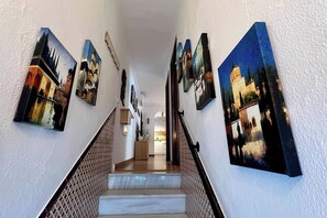 Un couloir avec un escalier menant à une pièce, dont les murs sont ornés de nombreux tableaux encadrés.