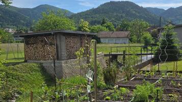 Paisaje rural con una construcción de piedra, un jardín cercado y montañas al fondo.