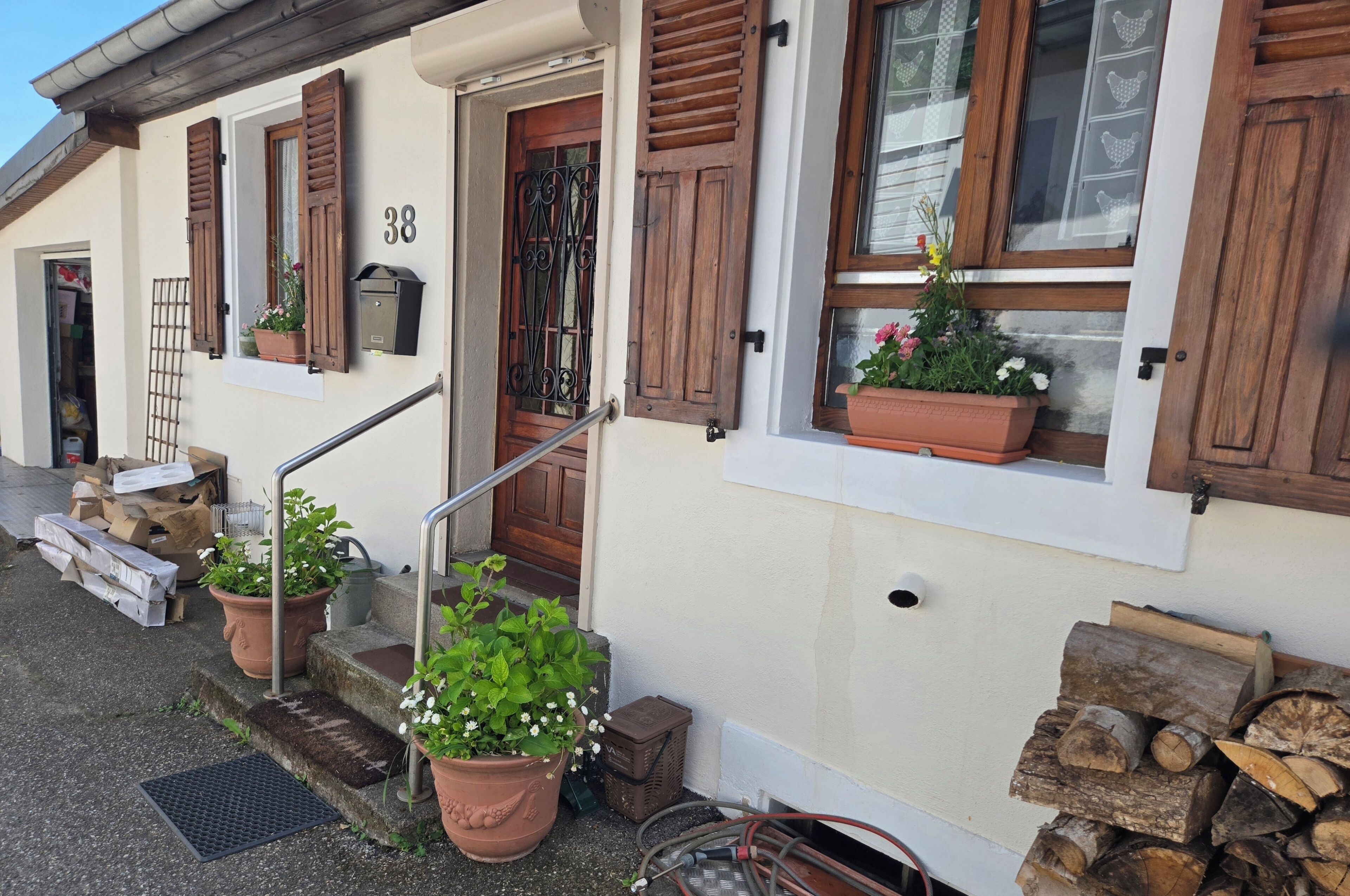 A building with a white facade, wooden shutters, and potted plants on the windowsills.