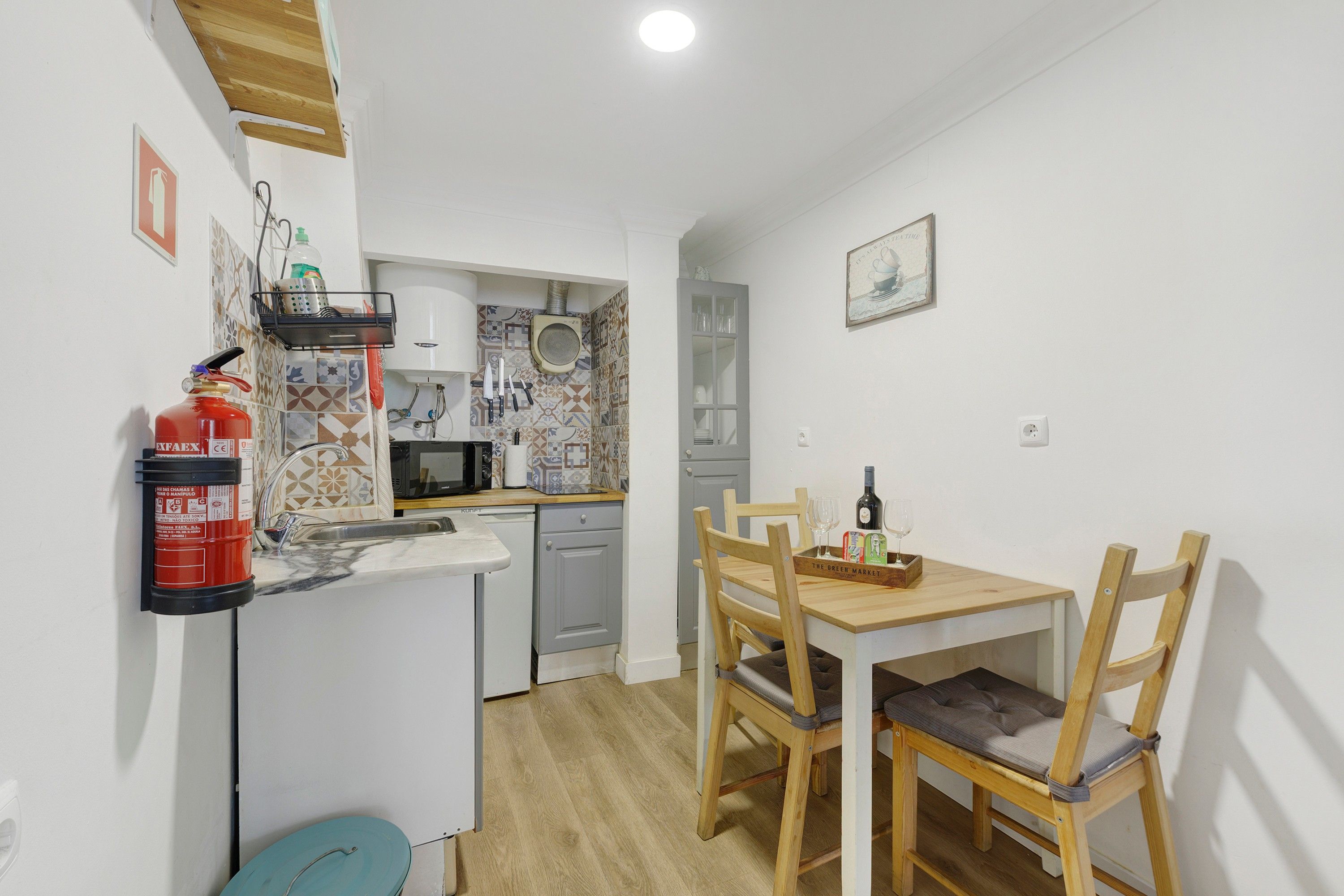 Een functionele keuken met een spoelbak, magnetron en een klein eethoekje met een houten tafel en stoelen.