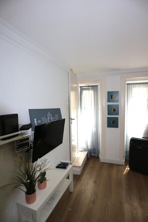 A modern living room with a flat-screen TV, a desk with a computer, a potted plant, and a window with curtains. - Central Apartment "Casa Dos Lagares" (Lisbon)