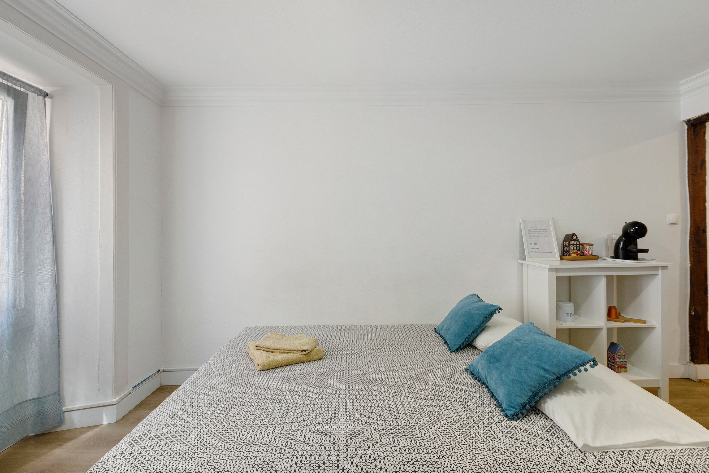 A bedroom with a bed, pillows, a nightstand, and a shelf with items.