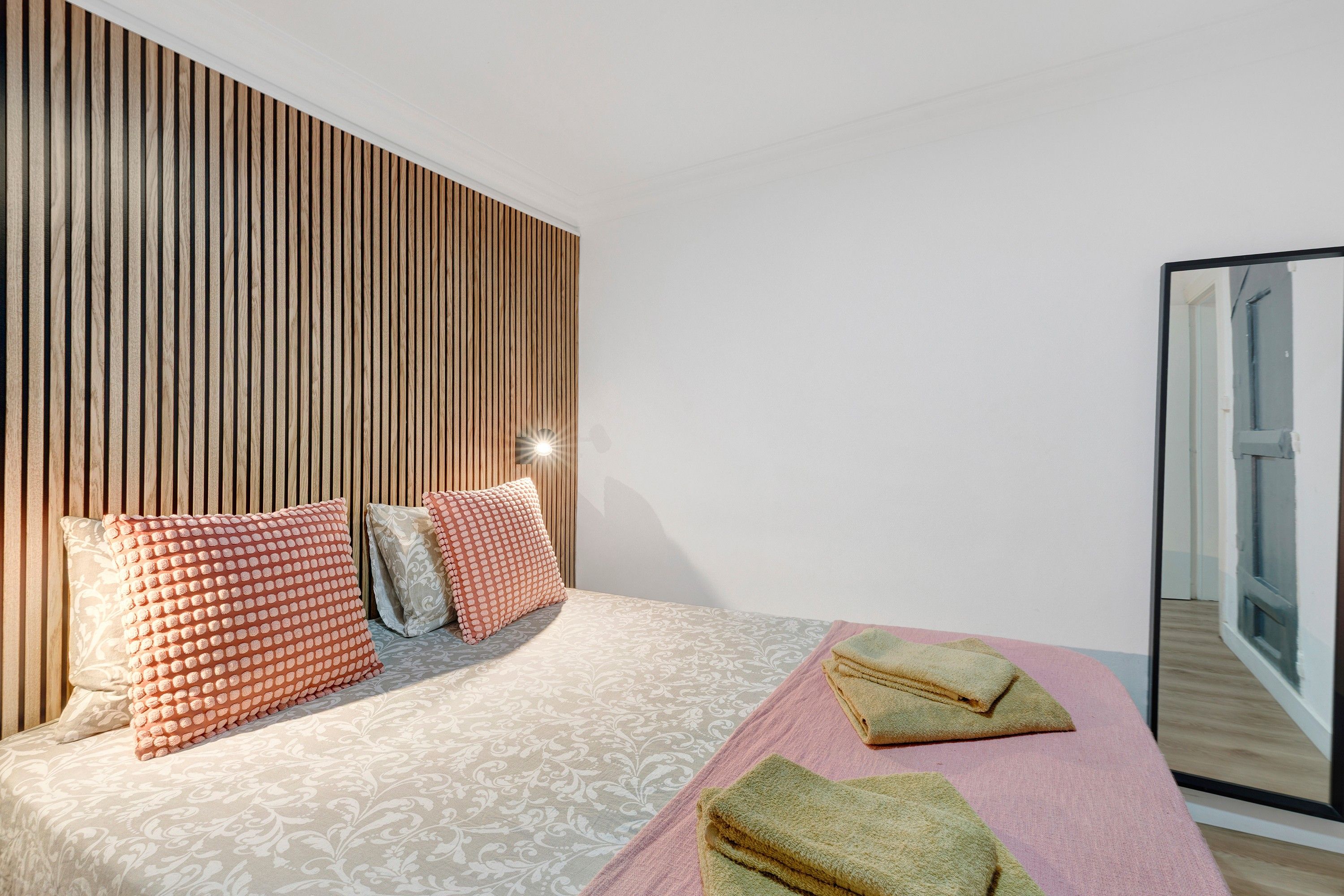 A modern bedroom with a wooden headboard, a patterned bedspread, and two towels on the bed.