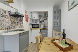 A compact kitchen with a sink, microwave, and a small refrigerator. There is a dining table with a bottle of wine and glasses. - Central Apartment "Casa Dos Lagares" (Lisbon)