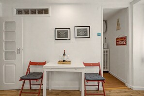 A room with a white table and two red chairs, a framed sign on the wall, and a bottle of wine on the table. - Casa Beco Do Castelo (Lisbon)