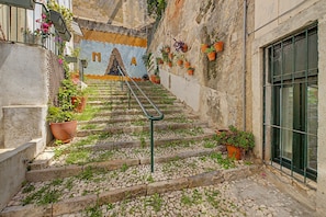 A staircase with a metal handrail leading to a door, surrounded by potted plants and a mural with large letters. - Casa Beco Do Castelo (Lisbon)